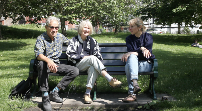 A man and two women sat on a bench in a park.