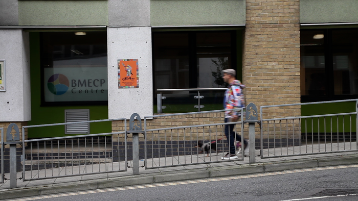 A photo of a man walking downhill past a building.