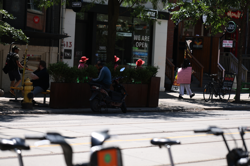 A walk with a playful question, 'To cake or not to cake?', invited pedestrians and patio patrons at the popular destination of King and Portland to reflect within a space largely defined by consumerism, in response to Score 4 created by Mushtari Afroz.
The walk was led by Mushtari, with the question displayed on a piece of pink art paper hanging from her back as she strolled along the sidewalk, carrying a piece of cake on a tray in her hand.
