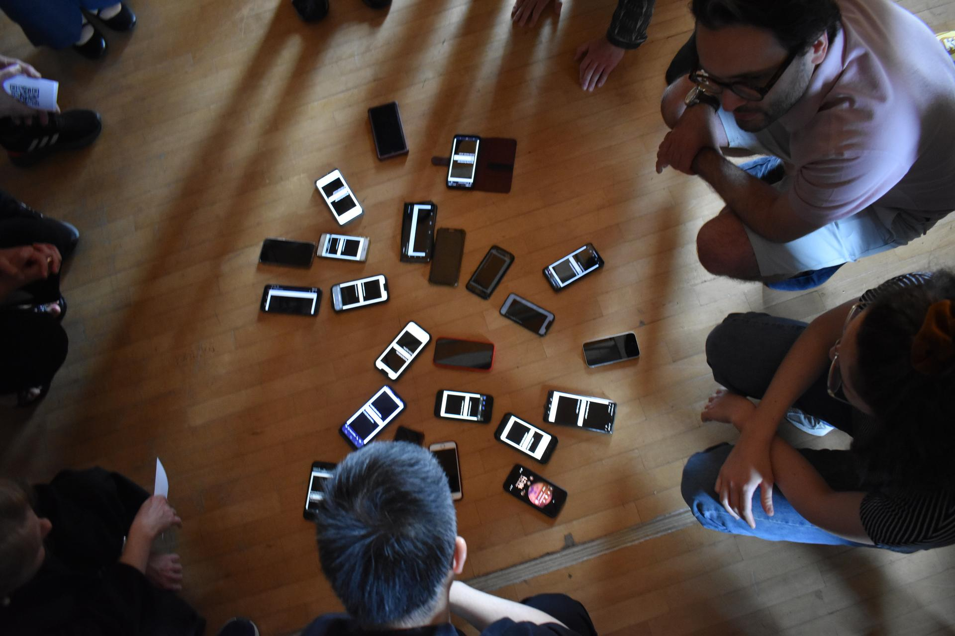 A group of people bend over cell phones lying on the floor and form a circle.