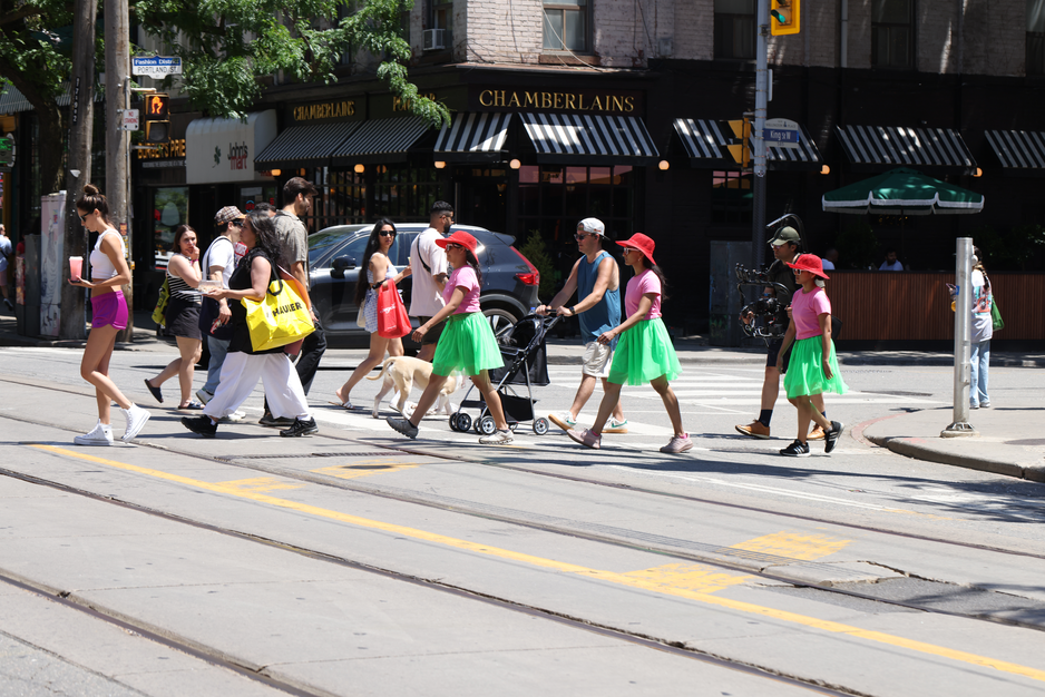 A walk with a playful question, 'To cake or not to cake?', invited pedestrians and patio patrons at the popular destination of King and Portland to reflect within a space largely defined by consumerism, in response to Score 4 created by Mushtari Afroz.
The walk was led by Mushtari, with the question displayed on a piece of pink art paper hanging from her back as she strolled along the sidewalk, carrying a piece of cake on a tray in her hand.