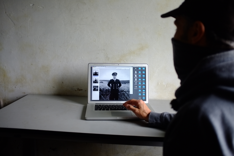 An open laptop pictures a figure dressed in Navy uniform. A man, partially visible, is looking at the laptop