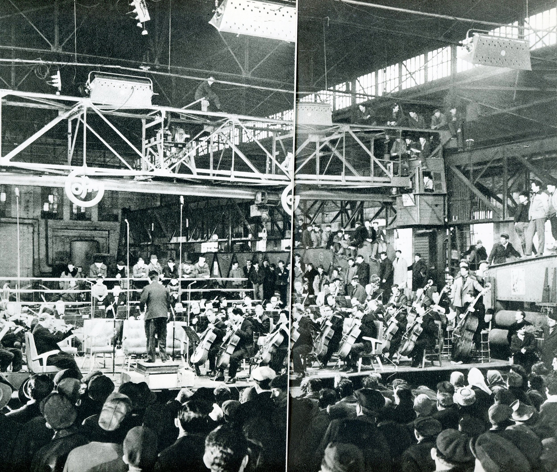 A black and white photograph of the Belgrade Philharmonic performing in Gosa factory. The musicians and conductor are on stage, the audience is standing surrounding the stage.