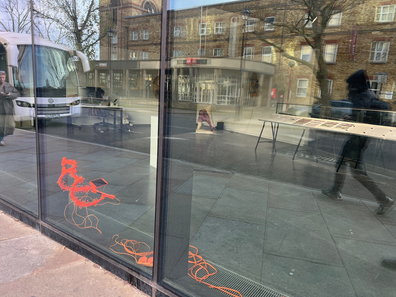 image of artwork view from outside the gallery through large plate glass windows. The objects are bright orange