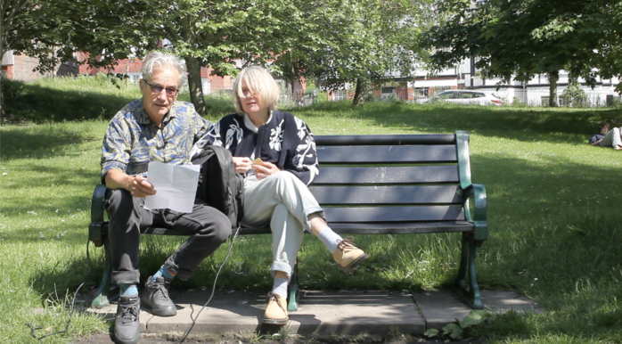 A man and a woman sat on a bench in a park.