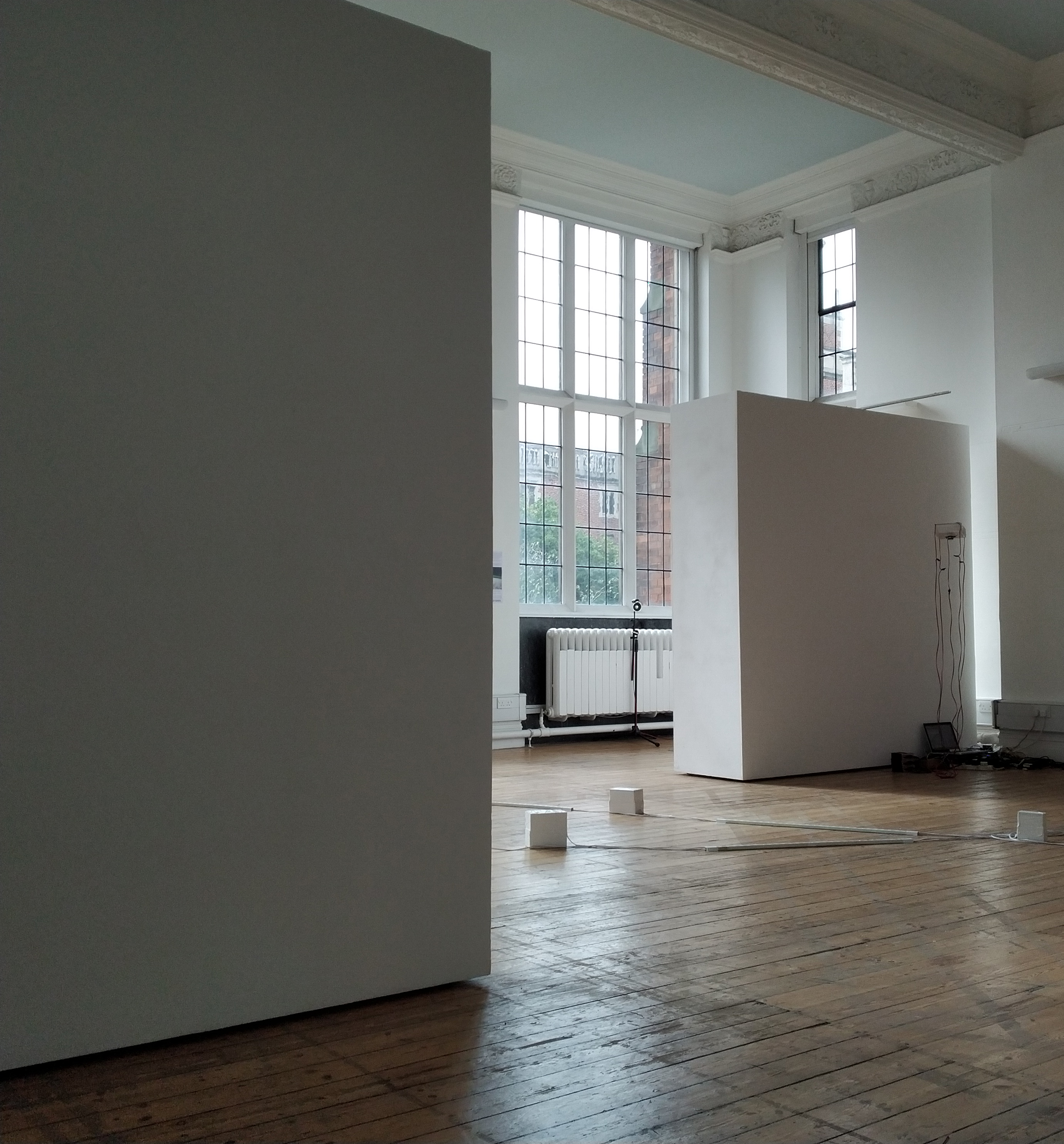 Tall largely empty room with wooden floors. A few small sculptures are present, to the edges of the image, suggesting that there is more just out of view.