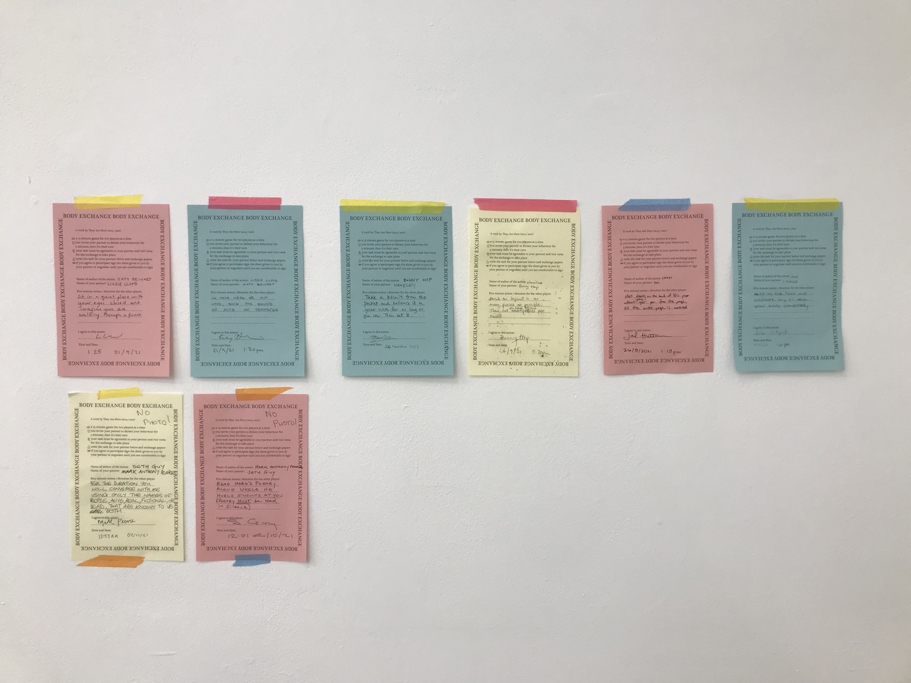 A photo of a wall with pieces of pink, yellow and blue paper taped it.