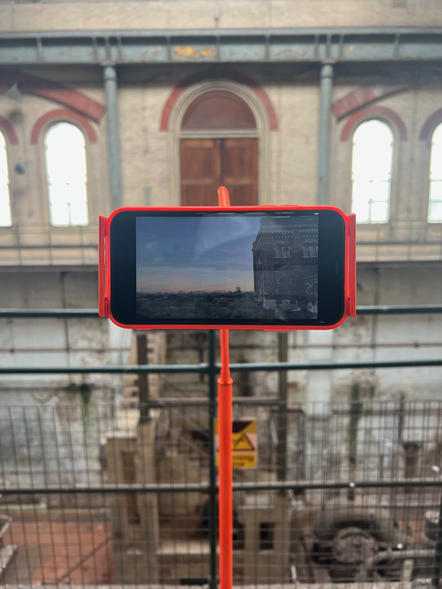 a detail of orange mobile phone with triple expansion house behind