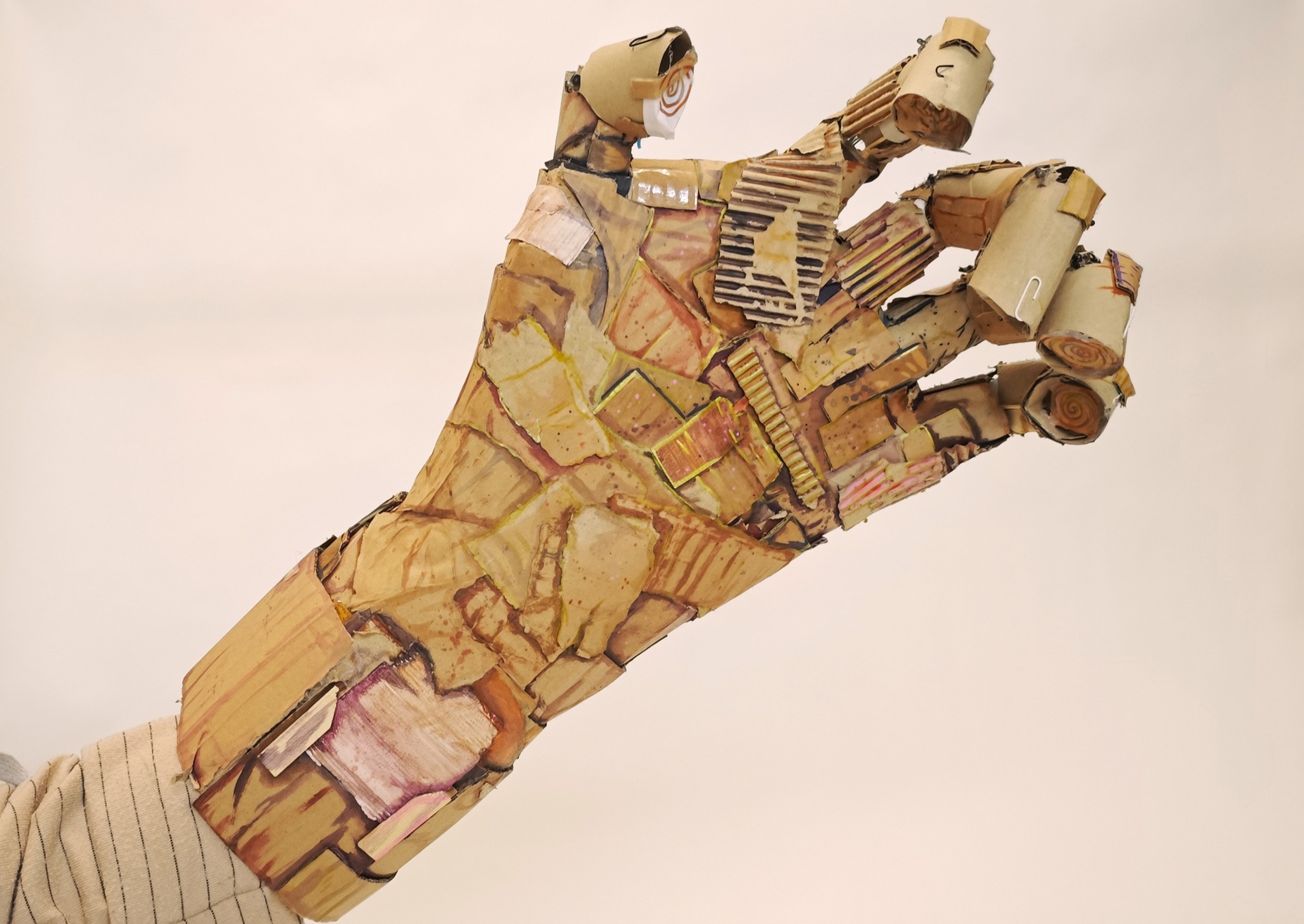 Artistic work of a hand made from cardboard scraps and small paper clips, predominantly in shades of brown.