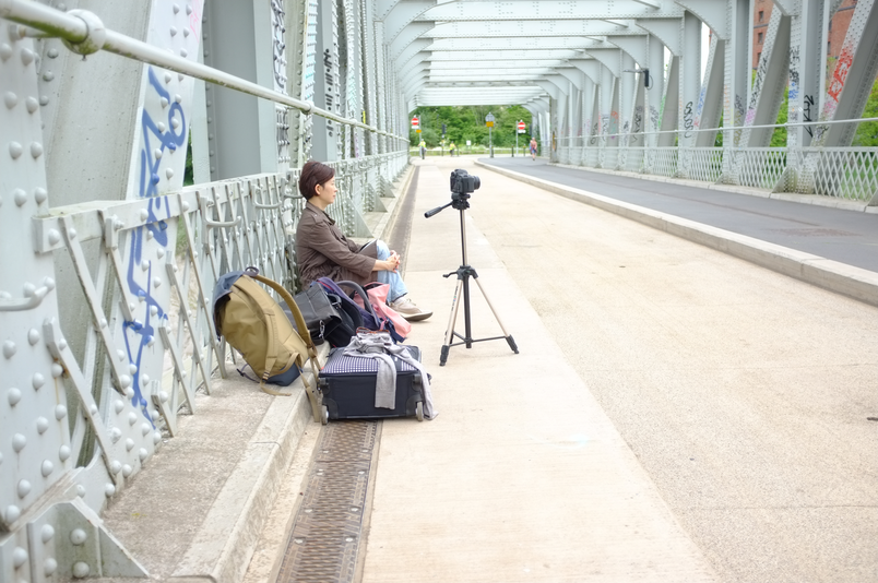A South Korean Woman sits on the ground of an iron bridge surrounded by recording equipment