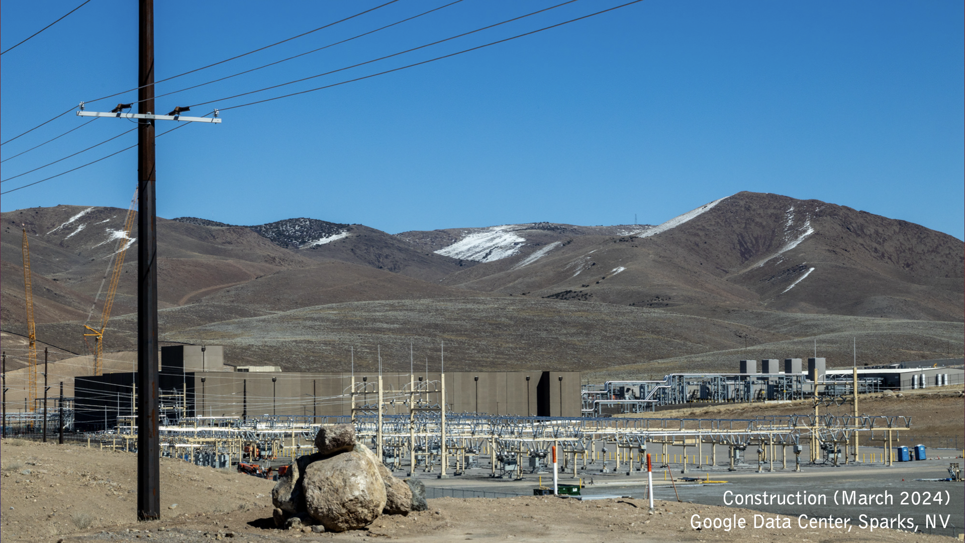 A conference room in the Google Headquarters with emtpy chairs and pictures hung up on the wall. A beamer projects a picture of the Google Headquarter Campus on a screen on the left. A TV screen on the right shows the words "Hello, Mountain View, Google Visitor Experience" on a colorful background.