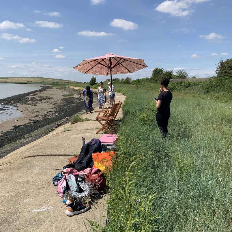 4 women pictured alongside an estuary with a pink parasol and lots of bags and recording equipment
