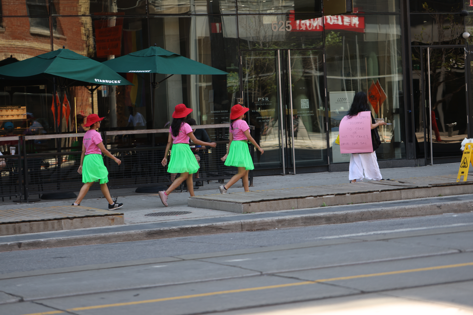 A walk with a playful question, 'To cake or not to cake?', invited pedestrians and patio patrons at the popular destination of King and Portland to reflect within a space largely defined by consumerism, in response to Score 4 created by Mushtari Afroz.

The walk was led by Mushtari, with the question displayed on a piece of pink art paper hanging from her back as she strolled along the sidewalk, carrying a piece of cake on a tray in her hand.