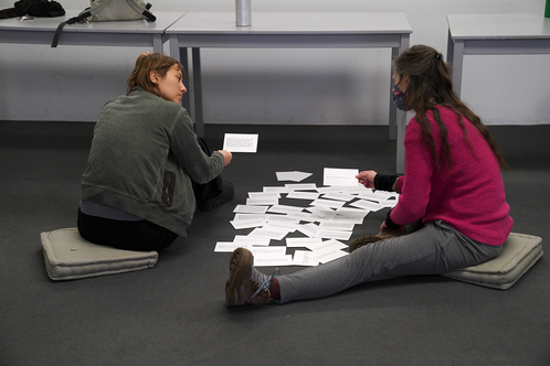 Two participants sit on the floor and discuss scenario cards.