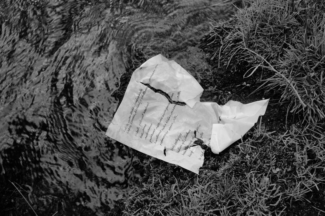 Järvivedessä kelluu jo hieman hajonnut paperi, jolle on kirjoitettu runo.
