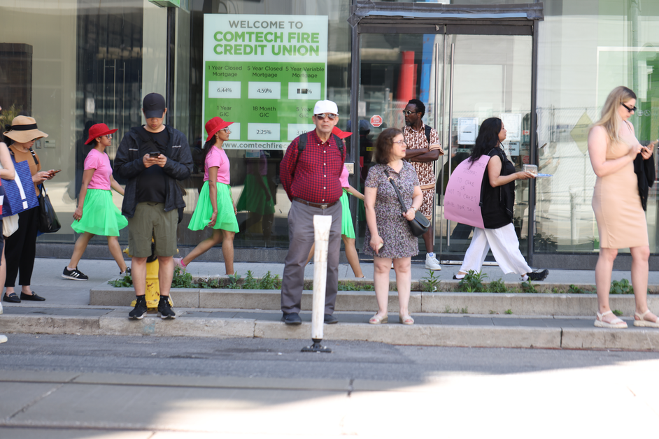 A walk with a playful question, 'To cake or not to cake?', invited pedestrians and patio patrons at the popular destination of King and Portland to reflect within a space largely defined by consumerism, in response to Score 4 created by Mushtari Afroz.

The walk was led by Mushtari, with the question displayed on a piece of pink art paper hanging from her back as she strolled along the sidewalk, carrying a piece of cake on a tray in her hand.