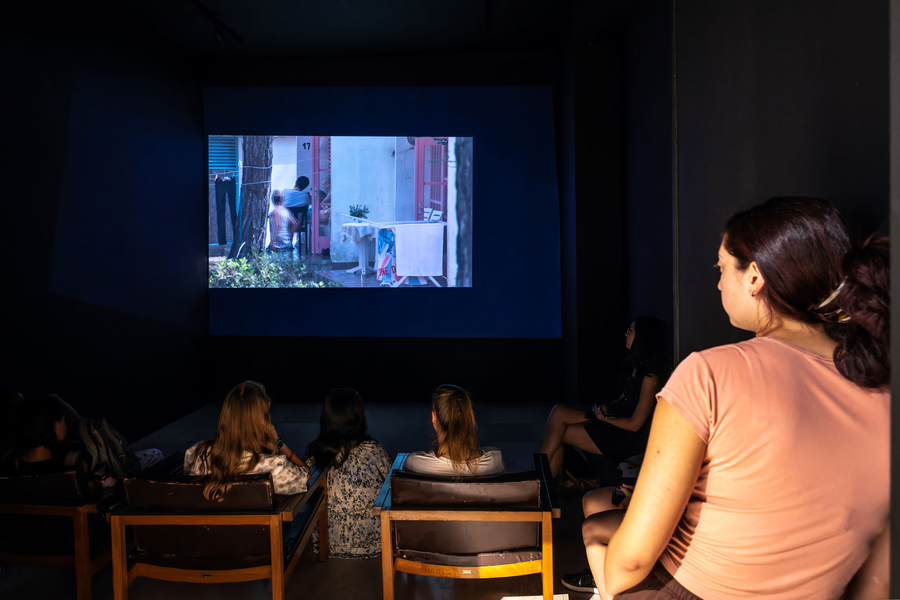 Photograph of teenagers sitting in a dark exhibition room and watching a video installation.