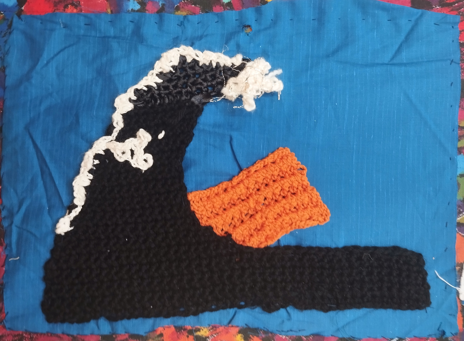 "No Life Raft will Persist under a Tsunami of oil", Material: blue background from Maker Space stash, crochet in black wool with white and silver added. Raft knitted in Indian Pillar stitch from cotton yarn