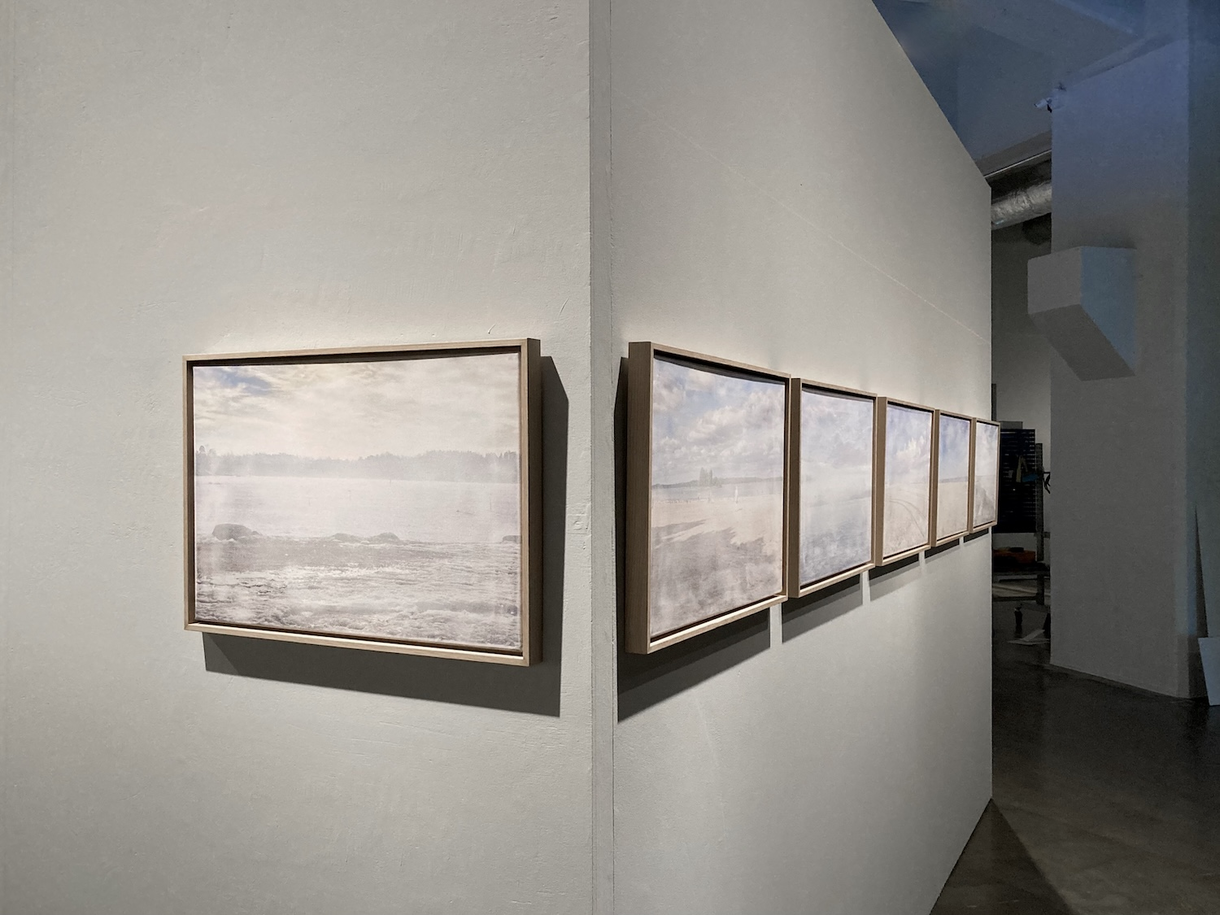 Yksityiskohta teoksesta Alt Text. Vierekkäin ripustettuja kehystettyjä ja vaaleita rantamaisemakuvia. Suomen Valokuvataiteen Museo 2022.