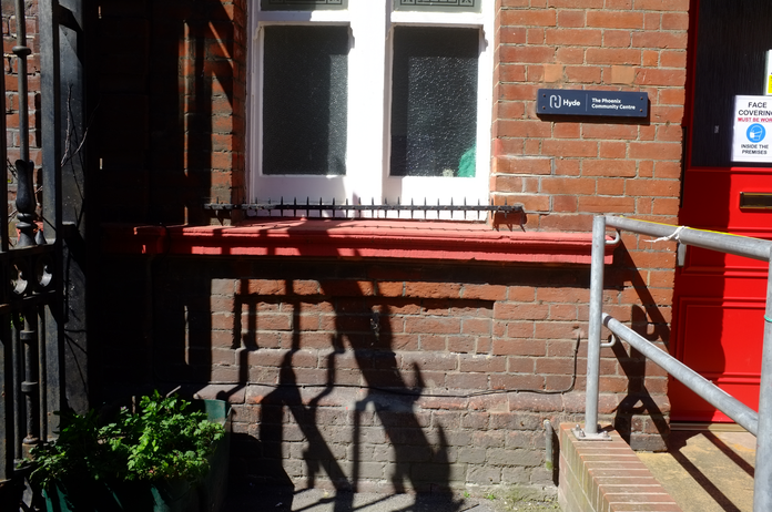 A photo of a red brick building with the shadow of some railings on the wall.