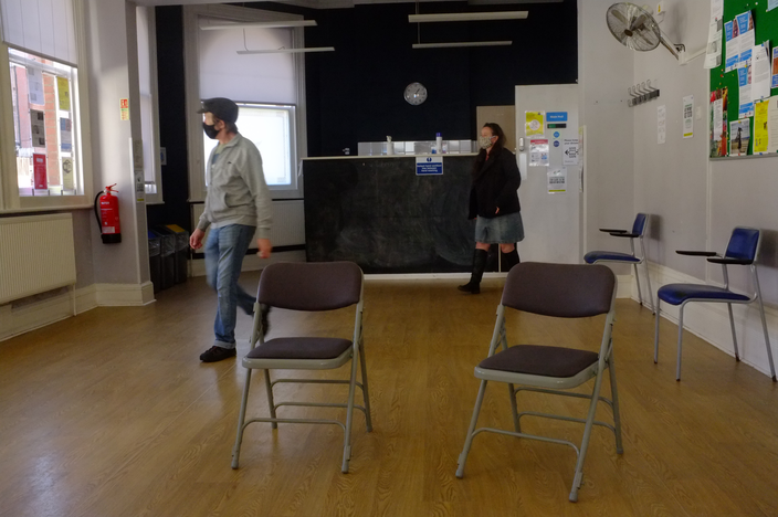 A photo of two chairs in the middle of a large hall and a man walking past.