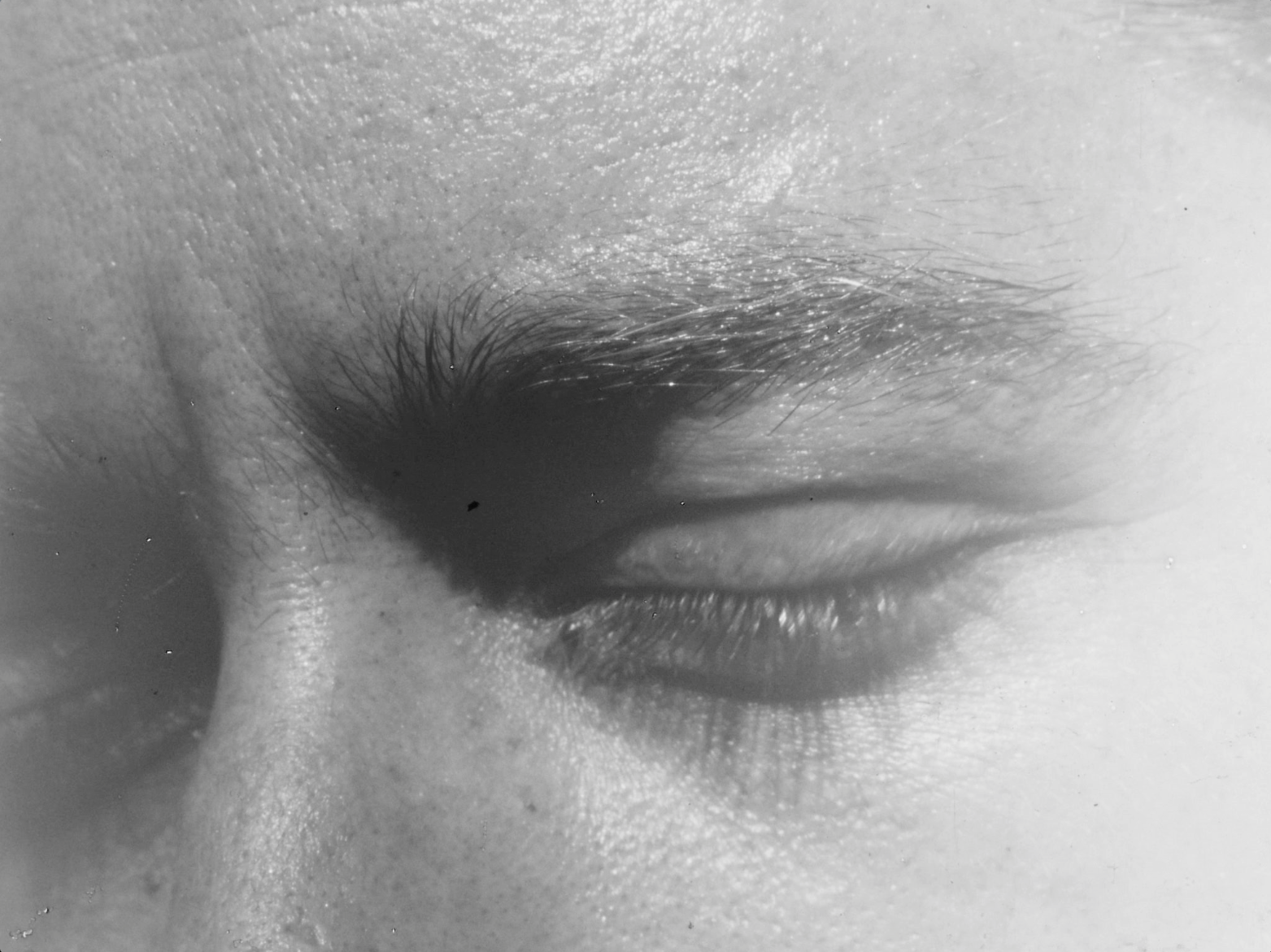 A black and white film still of Nazli Dincel's 16mm work, Instructions on How to Make a Film. You see a close-up of a face with closed eyes.
